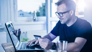 Homem sentado de frente para um computador para solicitar um cartão de crédito com o nome sujo.