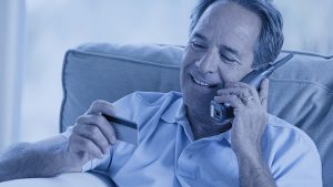 Foto de um homem falando no telefone celular e segurando um cartão carrefour na outra mão.