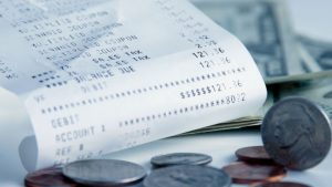 Nota fiscal paulista dobrada, com informações sobre a compra, ao lado de algumas moedas.