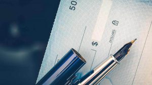 Imagem recortada de um cheque e de uma caneta.