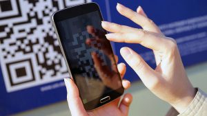 Foto da mão de uma pessoa segurando um celular para escanear um QR COde no Cinemark por meio do App Mercado Pago.