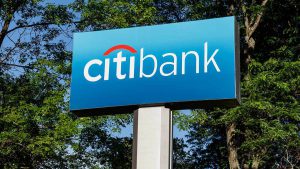 Imagem com uma paisagem de arvores, céu azul e uma placa em azul escrita Citibank.
