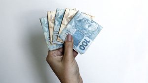 Mão feminina segurando notas dobradas de R$ 100 e R$ 50, representando o empréstimo pessoal da Sicredi.