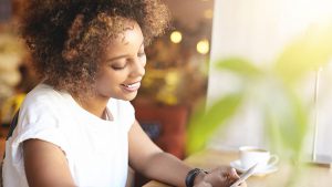 Mulher sorridente segurando e olhando para um aparelho celular, como se estivesse cadastrando o Internet Banking da Caixa.