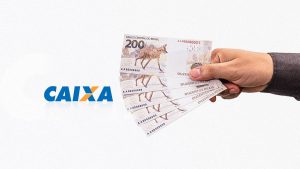 Mão masculina segurando notas de R$ 200 e, ao lado esquerdo, o logotipo da Caixa Econômica Federal.