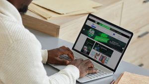 Imagem de um homem mexendo em um notebook, cuja tela apresenta o site da Havan.