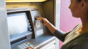 Mulher jovem em frente a um caixa eletrônico, inserindo um cartão no caixa para fazer um depósito no banco BRB.