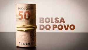 Notas de R$ 50 enroladas em um elástico e, ao lado direito da imagem, a escrita