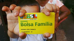 Criança segurando o cartão do Bolsa Família com as duas mãos.