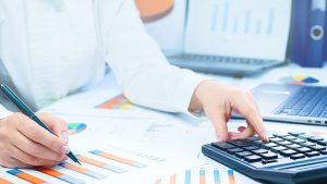 Foto de uma mulher sentada, usando uma calculadora para verificar se vale a pena contratar empréstimo para investir.