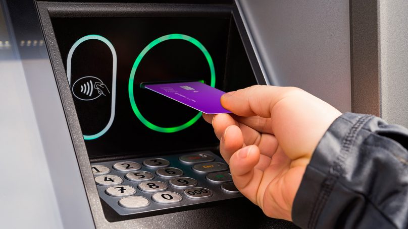 Imagem de uma mão inserindo o cartão de crédito Nubank em um caixa eletrônico, como se estivesse fazendo um saque.