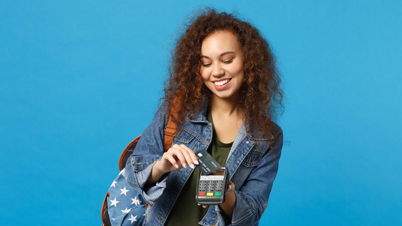 A imagem conta com um fundo azul e uma mulher passando seu cartão de acordo com a Taxas de Juros Maquininha Mercado Pago;