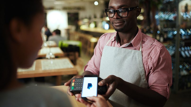 Mulher apontando a carteira digital PayPal na máquina de cartão para realizar o pagamento.