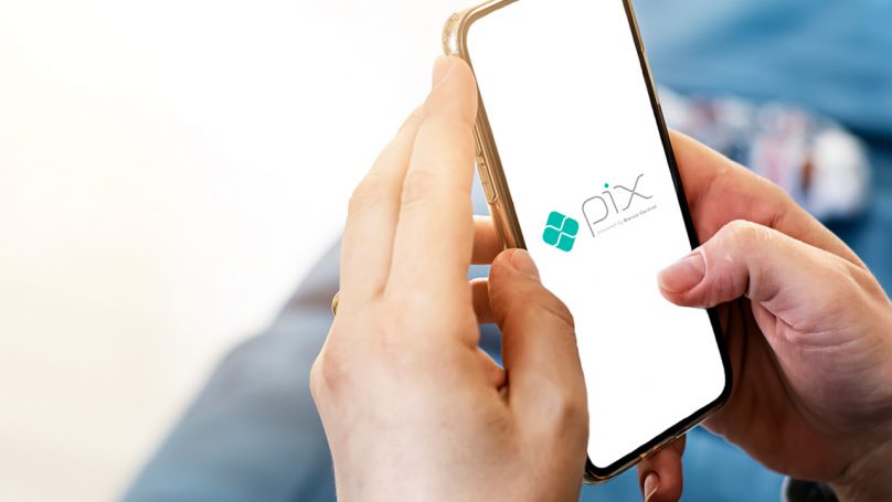 Mão masculina segurando um celular, cuja tela apresenta o aplicativo do Pix.