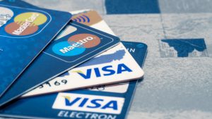 Quatro cartões de crédito, dois com a bandeira Visa e dois com a bandeira Mastercard, em cima de uma mesa.