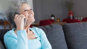 Imagem de uma mulher sorridente, com blusa azul, em uma ligação telefônica, como se estivesse conversando com um atendente do Banco Mercantil do Brasil.