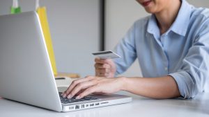 Homem mexendo no computador e segurando um cartão de crédito com a mão direita