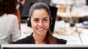 Foto de uma mulher sorrindo para a câmera, com um fone de ouvido com microfone, representando uma atendente da empresa Help! BMG.