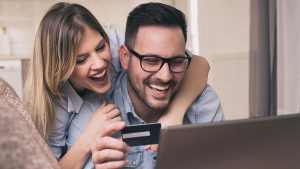 Casal sorridente, abraçado e olhando para a tela de um notebook. O homem está segurando um cartão de crédito preto, que representa o Cartão Senff.