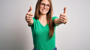 Imagem de uma mulher sorridente, de óculos, fazendo o sinal de