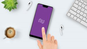 Mão feminina sobre a tela de um celular, que apresenta o logotipo do Nubank.