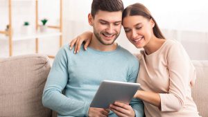 Imagem de um casal, composto por um homem e uma mulher, olhando para um tablet e sorrindo, como se estivessem consultando a taxa de juros do empréstimo consignado Itaú.