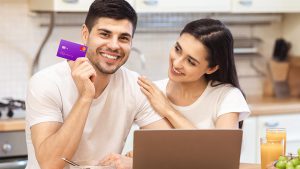 Casal composto por homem e mulher sorrindo para a foto. O homem está segurando um cartão de crédito Nubank.