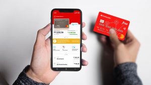 Imagem de uma pessoa segurando um celular, cuja tela mostra o aplicativo Santander Way e, ao lado direito, o cartão Santander.