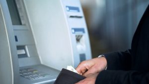 Pessoa mexendo na carteira, de frente para um caixa eletrônico, como se estivesse sacando dinheiro da conta salário do Banco do Brasil.