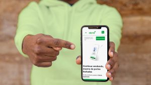 Homem com um moletom verde apontando para um celular, que mostra a tela da conta digital Stone.