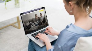 Foto de uma mulher branca usando um notebook. Na tela o site do programa de pontos Átomos.