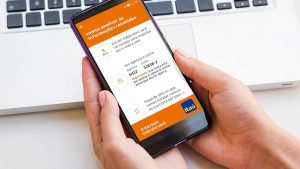 Foto da mão de uma pessoa segurando um aparelho celular. Na tela do aparelho está o aplicativo do banco Itaú, mostrando os serviços da conta Essencial.