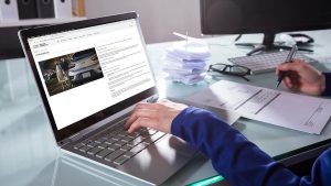 Imagem recortada de uma pessoa mexendo em um notebook e assinando um documento, como se estivesse emitindo a segunda via do boleto Chevrolet pela internet.