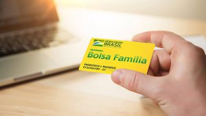 Mão masculina segurando o cartão do Bolsa Família na cor amarela e verde.