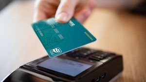 Pessoa segurando o cartão de crédito Banese Card e aproximando-o em uma maquininha.
