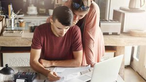 Homem e mulher olhando para um documento, de frente para um computador, como se estivessem consultando a fatura da Sky.