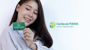Mulher jovem e sorridente segurando em suas mãos o cartão de Todos, na cor verde.