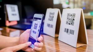Pessoa segurando o celular com o aplicativo InterPag aberto e apontando a câmera para o QR Code de uma mesa