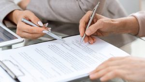 Duas pessoas com caneta na mão assinando um documento.