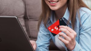 Mulher sorridente, com uma camisa azul, segurando o cartão de crédito Santander SX.