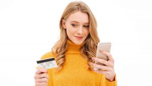 Mulher loira segurando um telefone celular em uma mão e na outra, um cartão de crédito.