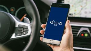 Homem dentro de um carro no lado do motorista, como se estivesse trabalhando no Uber, segurando um celular, que mostra o aplicativo do banco Digio.