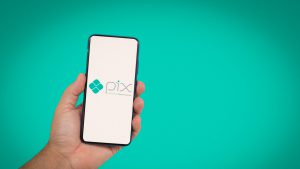 Mão masculina segurando um celular, cuja tela apresenta o aplicativo do Pix.