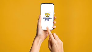Mão de uma pessoa segurando um celular. Na tela o App do Mercado livre, que também é do mesmo grupo que o Mercado Pago.
