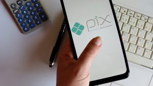 Mão feminina segurando um celular, cuja tela apresenta o logotipo do Pix.