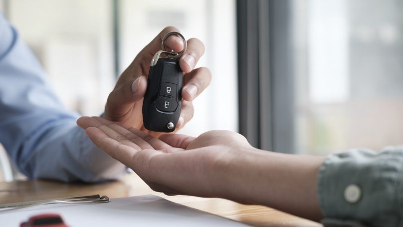Imagem de uma pessoa entregando a chave de um carro para outra, representando o financiamento de veículos Itaú.