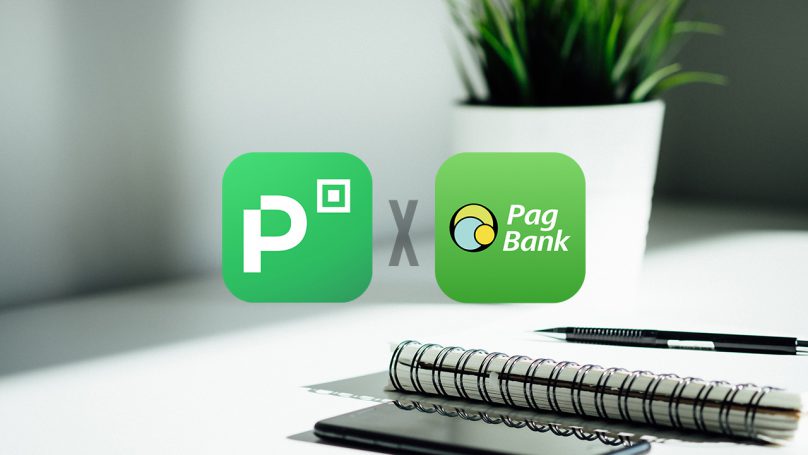 Na imagem é possível notar um vaso de plantas e uma mesa com cadernos acima, na frente estão os dois logos com um X no meio, indicando PicPay ou PagBank?