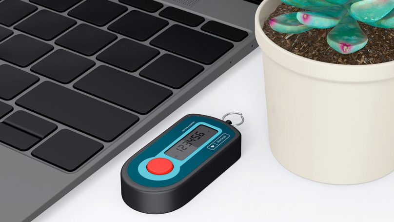 Notebook com teclado preto ao lado de um vaso de planta e de um token bancário.