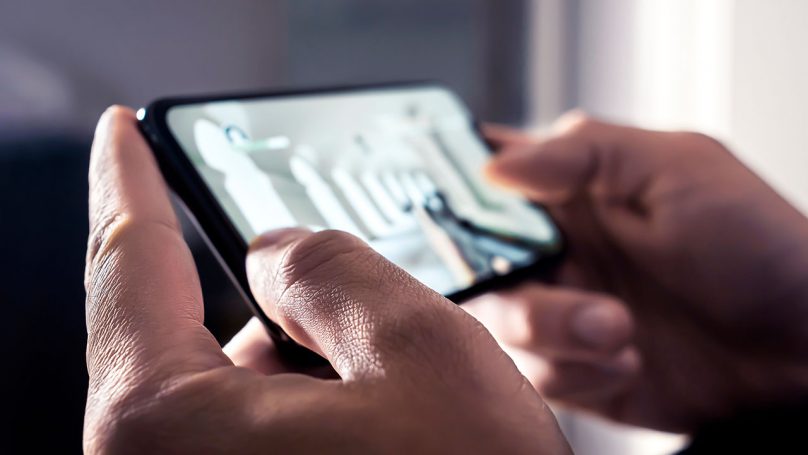 Adulto utilizando um celular, cuja tela apresenta a imagem de um jogo