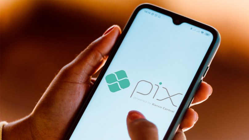 Mão feminina segurando um celular, cuja tela mostra o logotipo do Pix.